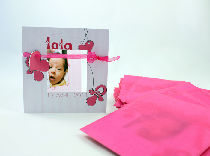 Faire-part Lola posé devant une pile d'enveloppes roses